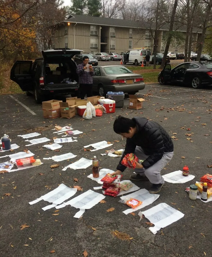 Grocery orders being sorted on a parking lot, the back of a car open beside them