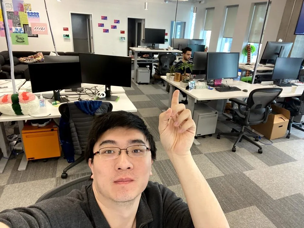 Yuzheng Sun taking a selfie in Facebook’s Seattle office, pointing up; posters on the wall behind him